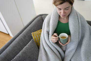 Woman wrapped in blanket drinking tea at home - SVKF01060