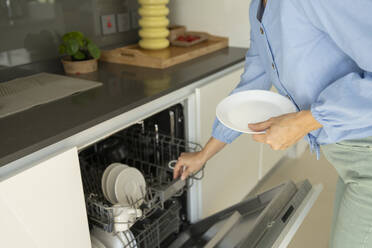 Hands of woman loading plates in dishwasher at home - SVKF01072