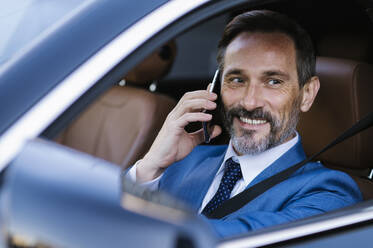 Smiling businessman talking through smart phone sitting in car - OIPF02742