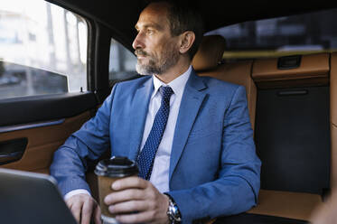 Nachdenklicher Geschäftsmann sitzt mit Einweg-Kaffeebecher auf dem Rücksitz eines Autos - OIPF02755