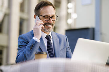 Senior businessman talking on smart phone sitting in cafe - OIPF02769