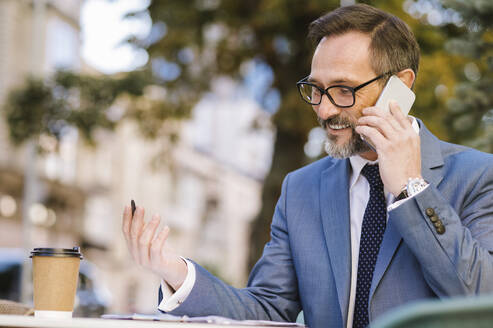 Glücklicher reifer Geschäftsmann im Gespräch über das Mobiltelefon bei der Arbeit im Cafe - OIPF02775