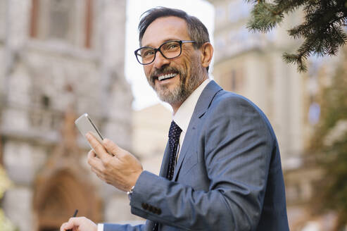 Glücklicher Geschäftsmann mit Brille und Smartphone - OIPF02777