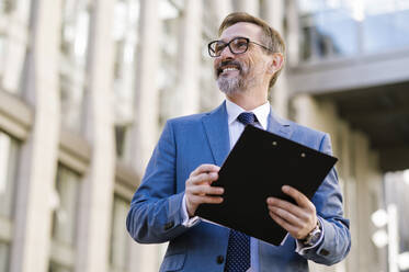 Happy businessman holding clipboard in front of building - OIPF02780