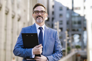 Contemplative mature businessman with clipboard outside building exterior - OIPF02781