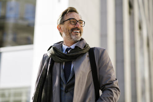 Glücklicher Geschäftsmann mit Brille steht vor einem Bürogebäude - OIPF02807
