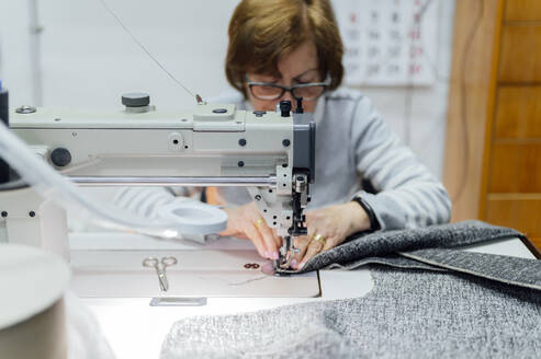 Senior craftswoman using sewing machine in workshop - PGF01435