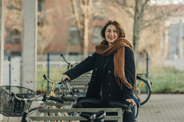Lächelnde reife Frau mit Fahrrad an einer Parkstation - VSNF00327