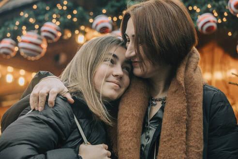 Glückliche Mutter mit Arm um Tochter auf dem Weihnachtsmarkt - VSNF00329