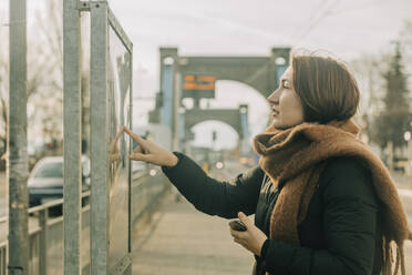 Mature woman checking arrival departure board at tramway station - VSNF00334