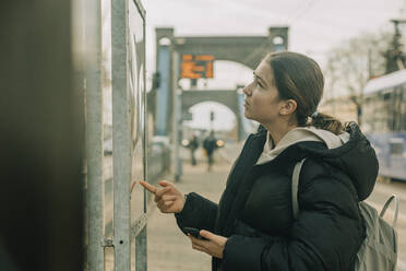 Teenage girl checking arrival departure board at tramway station - VSNF00335