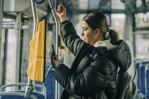 Teenage girl buying ticket through smart phone in tram - VSNF00344