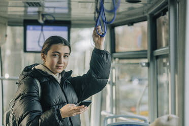 Smiling teenage girl standing with smart phone inside cable car - VSNF00345