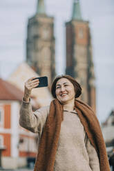 Happy mature woman taking selfie through smart phone - VSNF00348