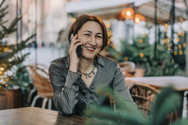 Glückliche reife Frau, die in einem Straßencafé mit einem Smartphone telefoniert - VSNF00351