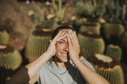 Smiling woman covering eye with hand on sunny day - DMGF00961