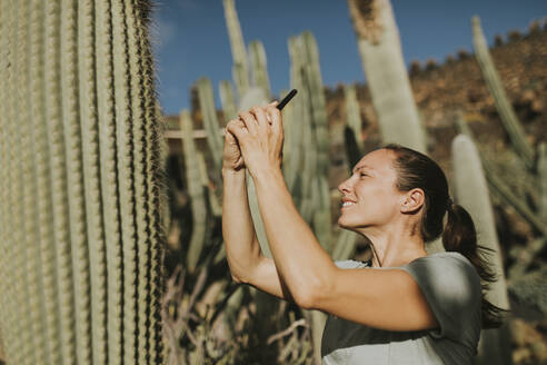 Glückliche Frau fotografiert Kaktus an einem sonnigen Tag - DMGF00962
