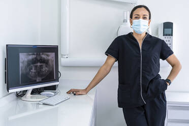 Doctor wearing surgical mask standing by desk at clinic - DLTSF03523