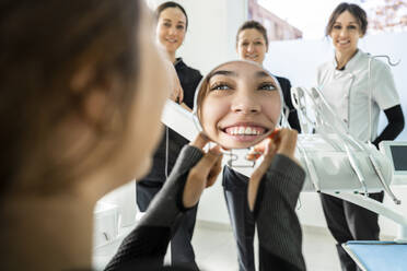 Happy patient holding mirror with female doctors standing in front at clinic - DLTSF03530