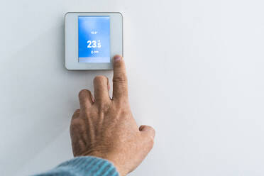 Hand eines Mannes beim Einstellen des Thermostats an der Wand - DLTSF03536