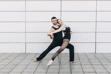 Couple with eyes closed performing dance in front of wall - JRVF03294