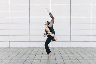 Man lifting woman upside down in front of tiled wall - JRVF03298