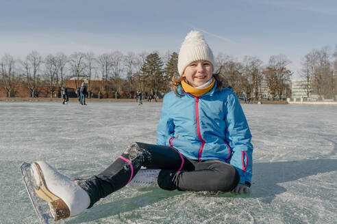 Glückliches Mädchen mit Strickmütze auf der Eisbahn sitzend - OGF01280