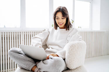 Happy young woman using laptop at home - MDOF00497