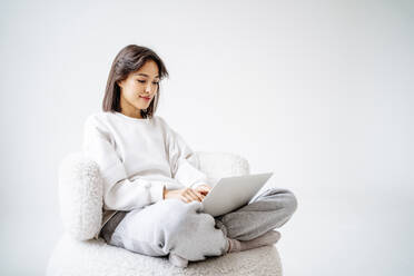 Junge Frau im Schneidersitz mit Laptop vor einer Wand - MDOF00498