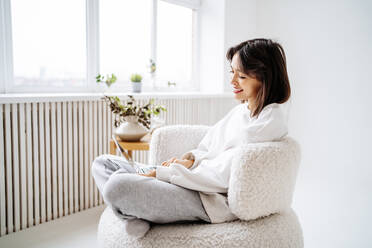 Young woman using laptop on chair at home - MDOF00499