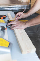 Hände eines Zimmermanns, der ein Holzbrett in der Werkstatt ausmisst - JAQF01205