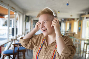 Nicht-binäre Person mit Kopfhörern, die in einem Café Musik hört - VRAF00009