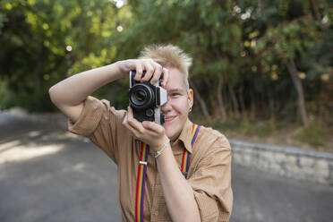 Nicht-binäre Person fotografiert mit Kamera im Park - VRAF00016