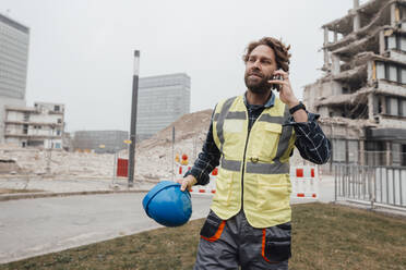 Älterer Arbeiter, der auf einer Baustelle mit seinem Smartphone telefoniert - JOSEF15725