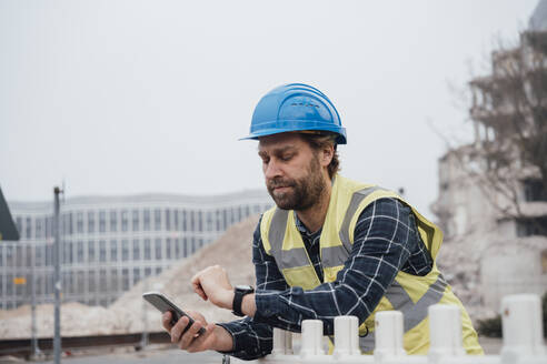 Älterer Arbeitnehmer mit Smartphone, der die Zeit auf seiner Smartwatch überprüft - JOSEF15745