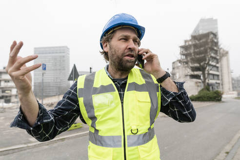 Frustrierter Arbeiter, der am Fußweg mit seinem Smartphone telefoniert - JOSEF15753