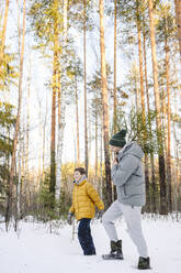 Happy son with father carrying pine tree in winter forest - EYAF02517