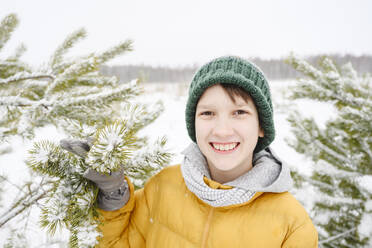 Happy boy holding pine tree in winter - EYAF02525