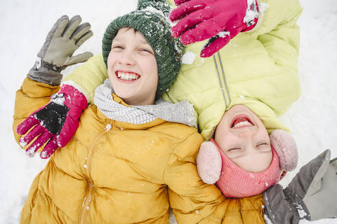 Fröhliches Mädchen mit Bruder, das sich im Schnee vergnügt - EYAF02527