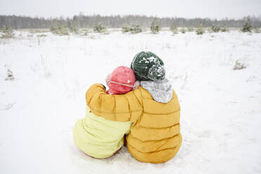 Bruder im Arm mit Schwester auf Schnee sitzend - EYAF02531