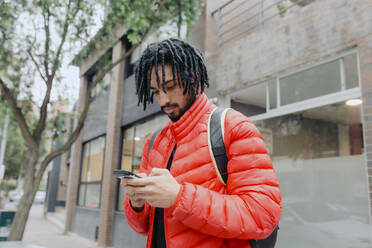 Man using smart phone standing in front of building - DSIF00657