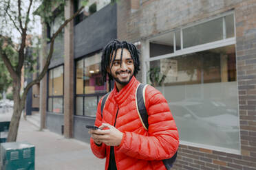 Lächelnder Mann mit Smartphone vor einem Gebäude stehend - DSIF00658