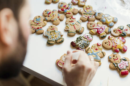 Man decorating gingerbread cookies on table - ONAF00388
