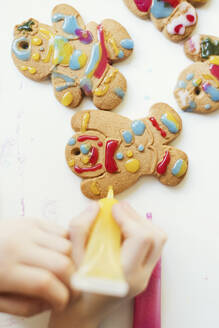 Hands of boy decorating gingerbread cookies on table - ONAF00389