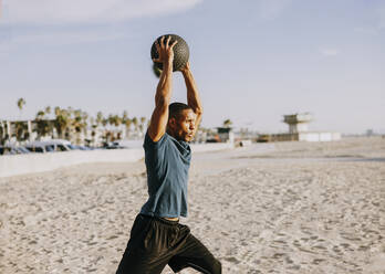 Älterer Sportler mit erhobenen Armen beim Training mit einem Ball am Strand - OIPF02817