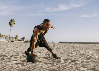 Älterer Sportler trainiert mit Medizinball am Strand an einem sonnigen Tag - OIPF02818