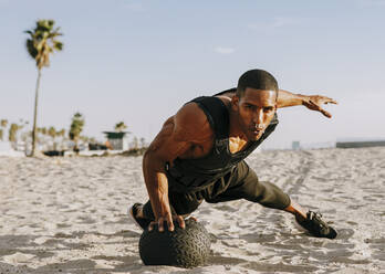 Sportler beim Training mit Medizinball am Strand an einem sonnigen Tag - OIPF02819