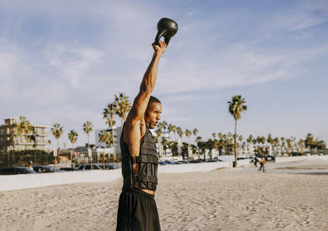 Älterer Sportler trainiert mit Kettlebell am Strand - OIPF02822