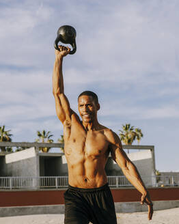 Aktiver Sportler beim Training mit der Kettlebell unter bewölktem Himmel - OIPF02832