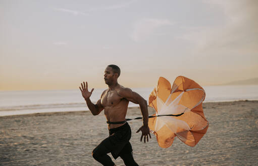 Sportler läuft mit Fallschirm vor dem Meer am Strand - OIPF02855